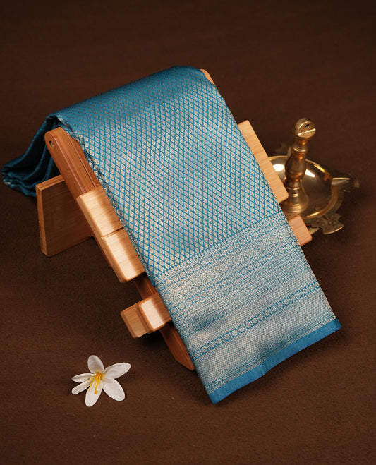 Teal blue colour semi soft silk brocade saree featuring delicate gold woven motifs across the body, enhanced with a self-colour intricately designed border and pallu, paired with a matching blouse piece.