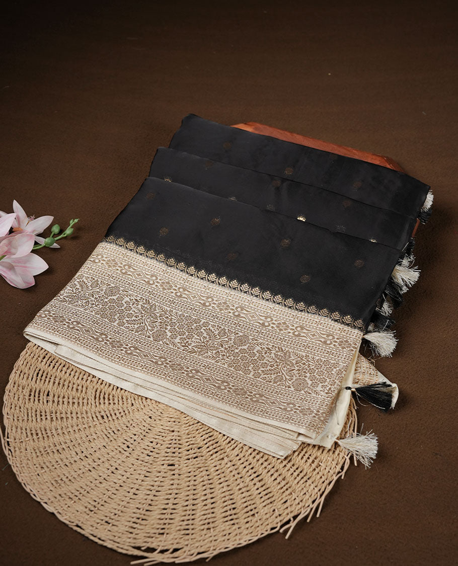 Black colour banaras satin crepe saree featuring gold zari motifs on body, with contrast cream colour border with gold zari pattern and paired with matching blouse.