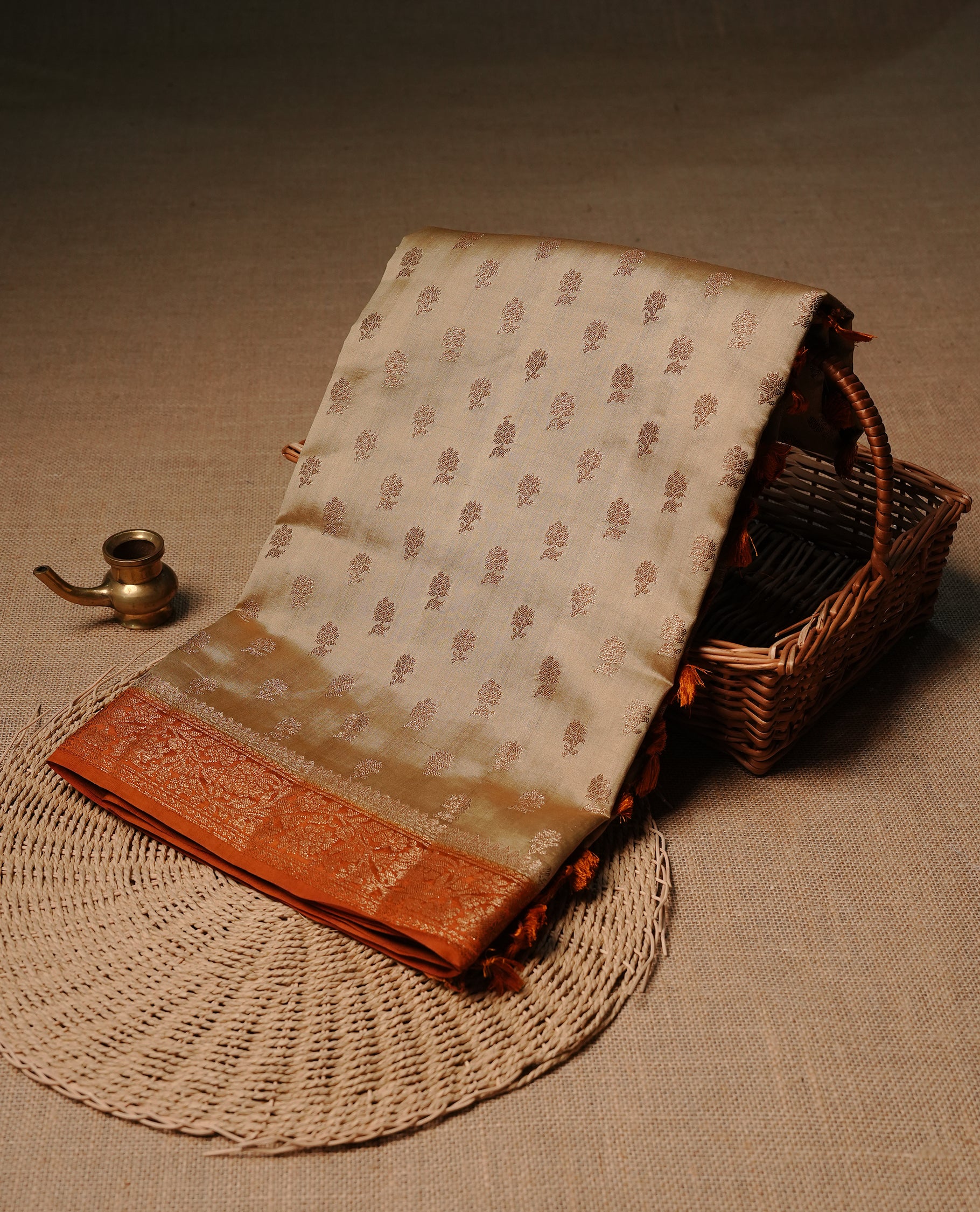 Cream colour pure tussar Banaras silk saree featuring intricate gold zari motifs across the body, enhanced with a contrast orange floral kodi zari border for a rich traditional look. Comes with a matching blouse piece.