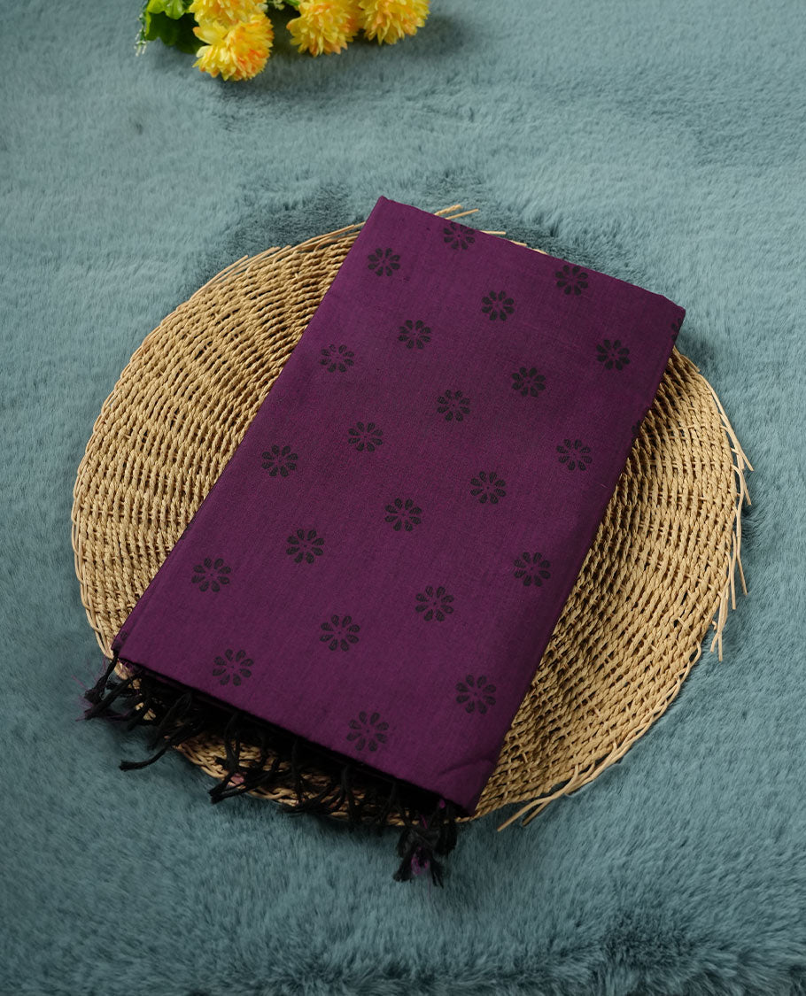 Grape Purple colour poly cotton saree with black floral butti motifs on the body, paired with a matching pallu featuring black ornate floral jaal and stripes on the border, and a coordinated all‑over black paisley printed blouse piece.