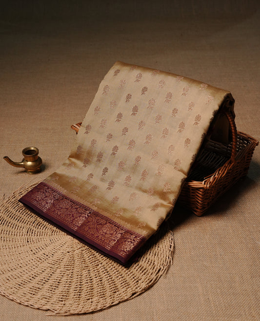 Cream colour pure tussar Banaras silk saree featuring intricate gold zari motifs across the body, enhanced with a contrast Maroon floral kodi zari border for a rich traditional look. Comes with a matching blouse piece.