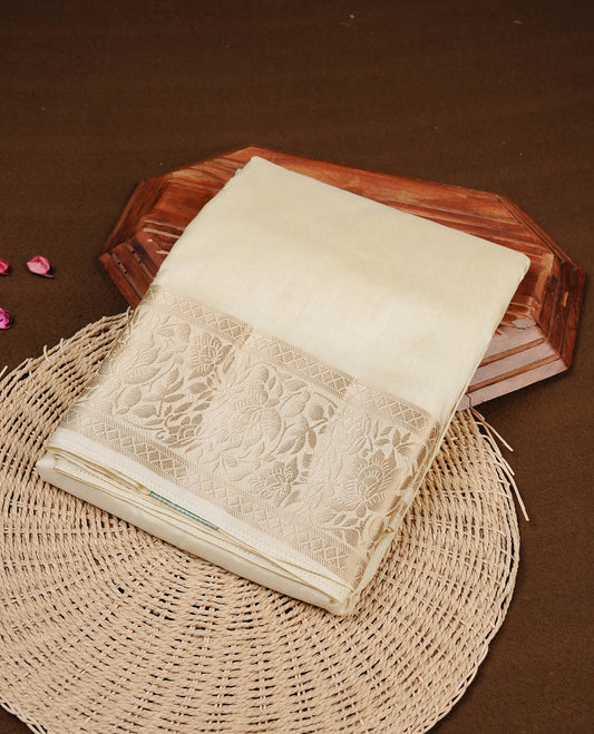 Cream colour semi Tussar silk saree featuring an elegant plain body, complemented by a self colour border adorned with traditional gold zari floral kodi patterns. Comes paired with a matching blouse piece.