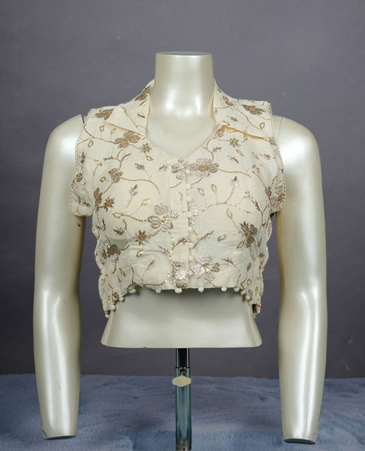 Cream embroidered sleeveless blouse with delicate floral threadwork, front buttons, and soft pom-pom hem detailing.