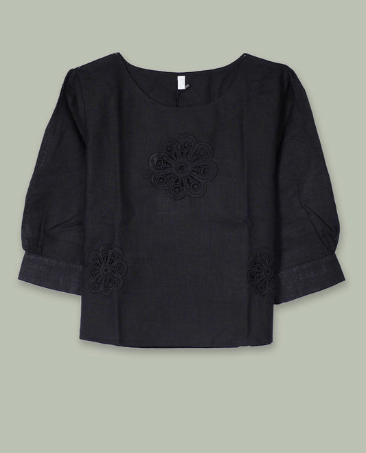 Black three-quarter sleeve top with round neckline and tonal crochet floral appliqués placed at the center front and near the hem.