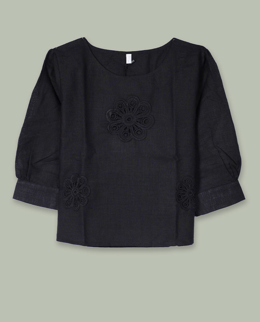 Black three-quarter sleeve top with round neckline and tonal crochet floral appliqués placed at the center front and near the hem.