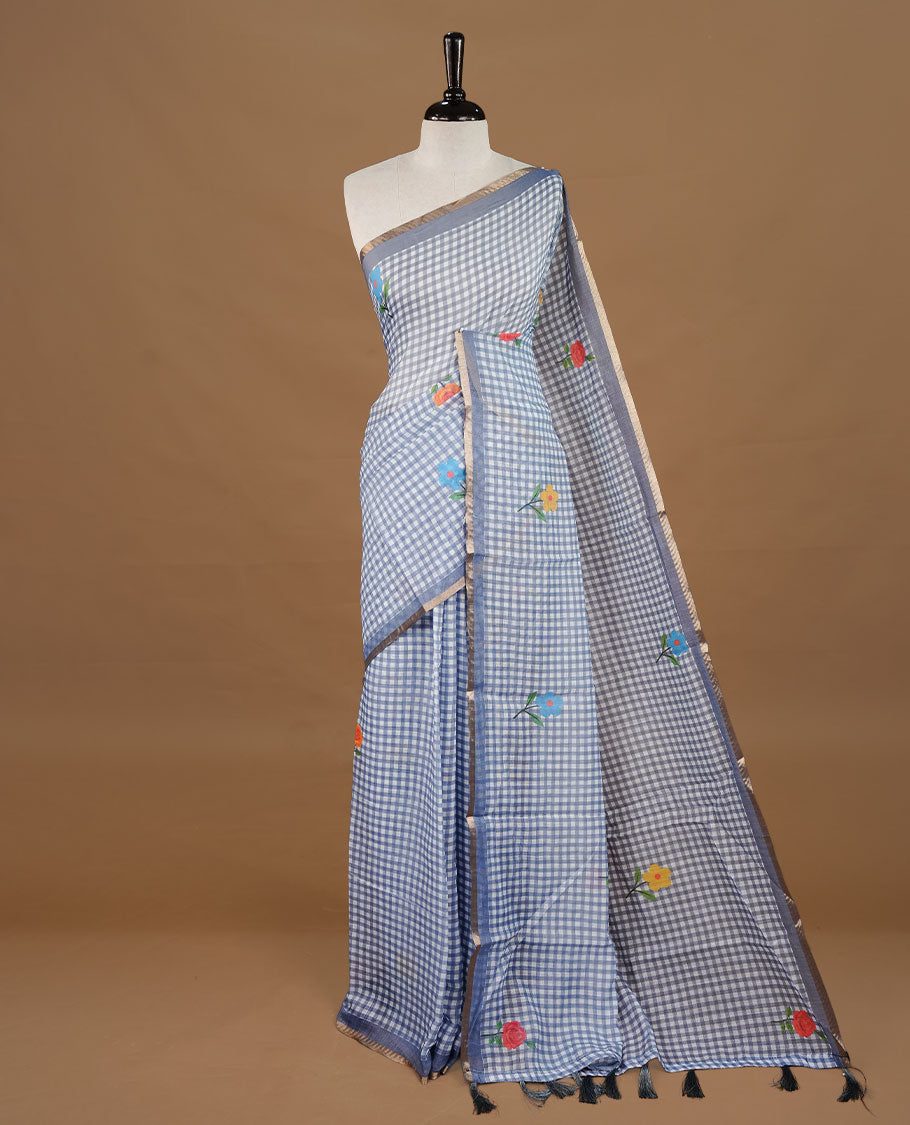 Grey colour Semi Linen saree featuring a stylish check pattern adorned with floral prints on the body, enhanced by a small gold border, paired with a matching blouse piece.