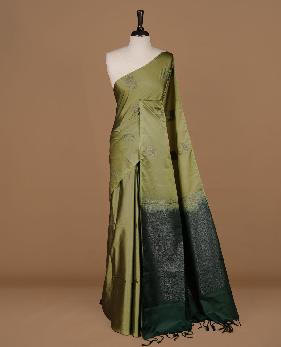 Olive colour soft silk saree features a sleek borderless design with intricate antique zari motifs, flowing into a striking contrast green pallu and a matching blouse piece.