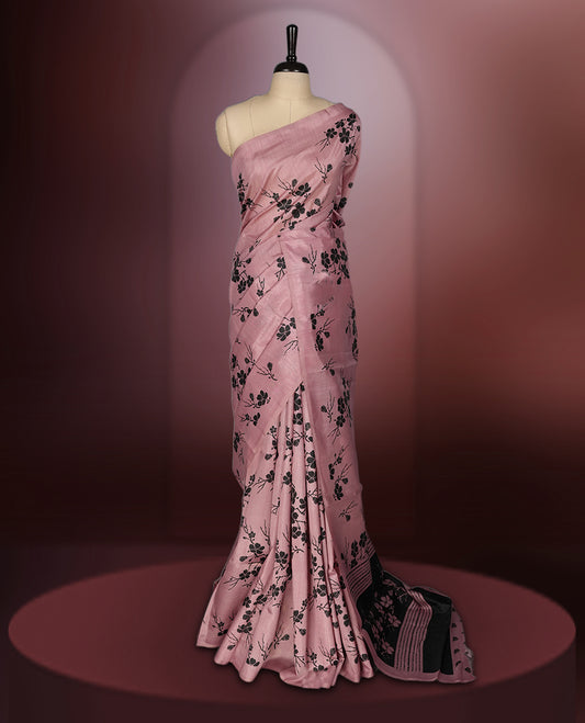 Pastel pink colour saree with black floral prints all over the body, complemented by a contrasting black pallu adorned with bold floral designs and striped detailing & Paired with a matching blouse for a complete look.