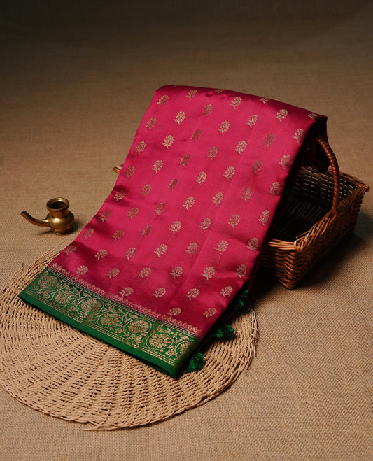 Magenta colour pure tussar Banaras silk saree featuring intricate gold zari motifs across the body, enhanced with a contrast green floral kodi zari border for a rich traditional look. Comes with a matching blouse piece.