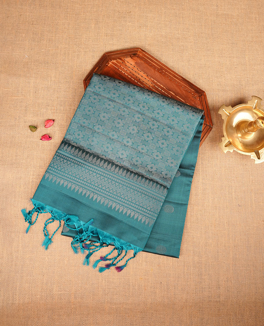 Teal colour soft silk saree featuring silver zari motifs on body, complemented by self colour with traditional border with tassel at pallu, paired with matching blouse piece.