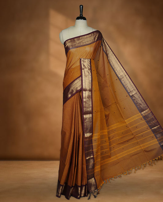 Mustard Brown colour chettinad cotton saree featuring plain body, paired with a black colour traditional gold zari border paired with matching blouse.
