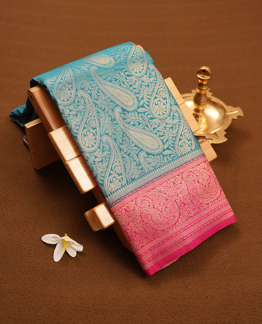Blue colour semi silk brocade saree featuring intricate Gold Floral kodi & leaf patterns across the body, complemented by a contrast Magenta colour woven border and pallu, paired with a matching blouse.