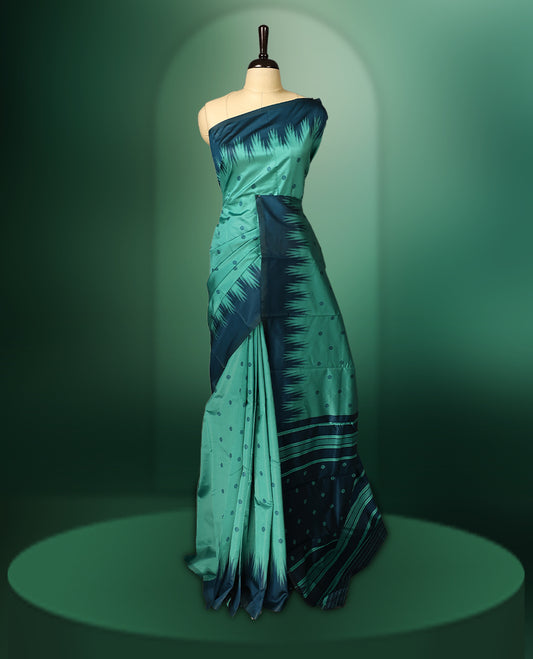 Sea green colour saree highlighted with subtle dotted motifs, complemented by a deep teal border featuring bold Ikat inspired patterns and striped pallu, paired with a matching blouse