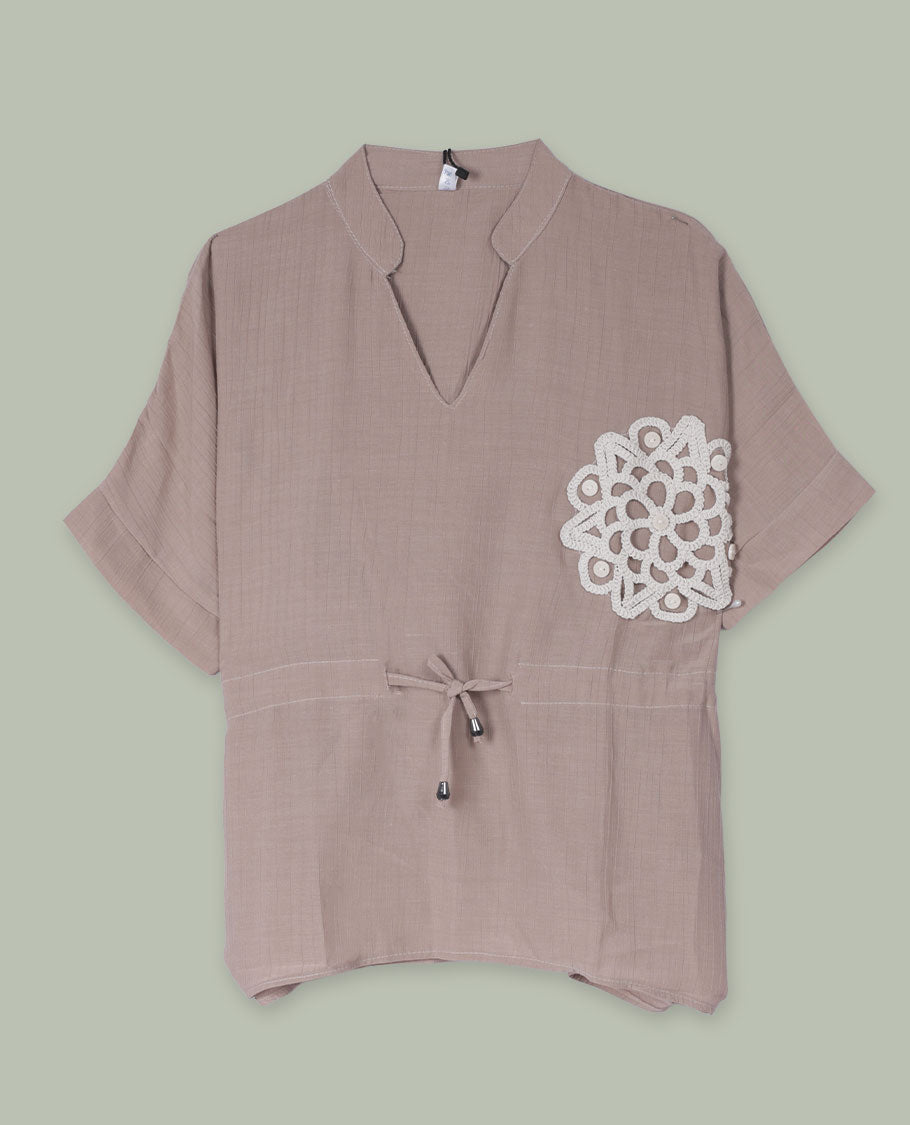 Taupe short-sleeve top with V-slit band neckline, contrast white crochet motif on one side, and adjustable drawstring detail at the waist