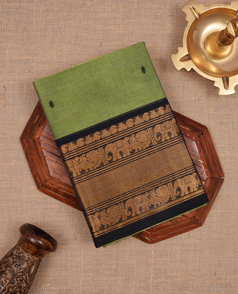 Green colour chettinad saree featuring gold zari motifs on body, complemented by contrast black colour with traditional border, paired with matching blouse piece.