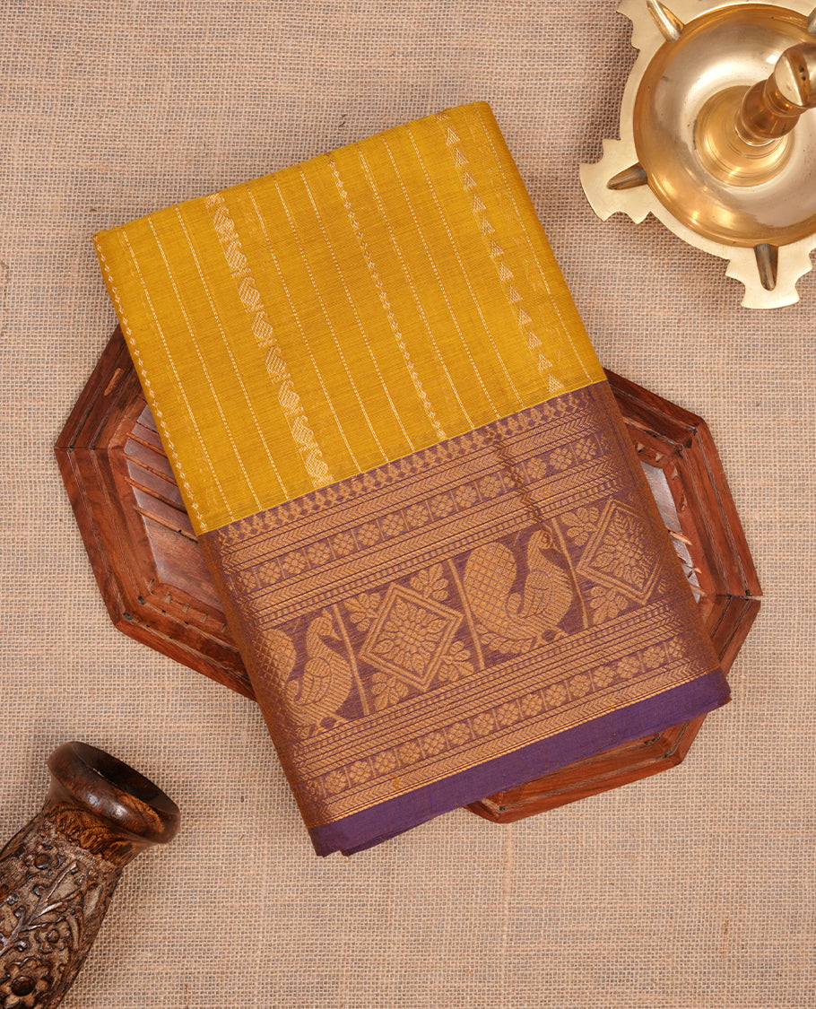 Olive yellow colour chettinad saree featuring gold zari motifs on body, complemented by contrast purple colour with traditional border, paired with matching blouse piece.