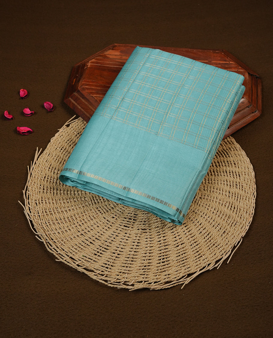 Powder blue colour semi Tussar saree highlights gold zari check pattern across body,  border, pallu and paired with matching blouse piece.