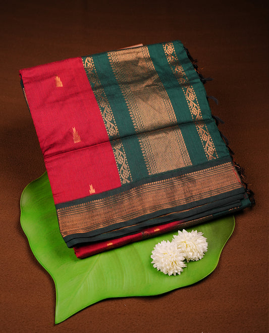 Dark maroon colour Kalyani cotton saree featuring delicate zari buttas on the body, complemented by a dark green zari border and woven pallu, paired with a matching blouse.