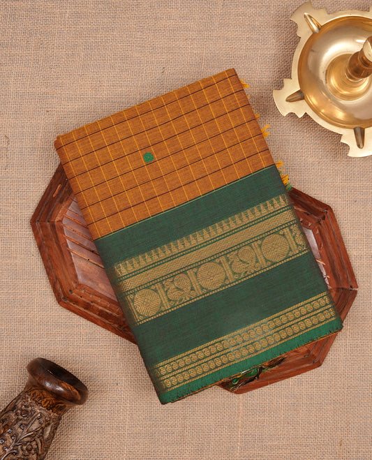 Mustard colour chettinad cotton featuring check pattern on body, complemented by contrast chocolate brown colour with gold zari border, paired with matching blouse piece.