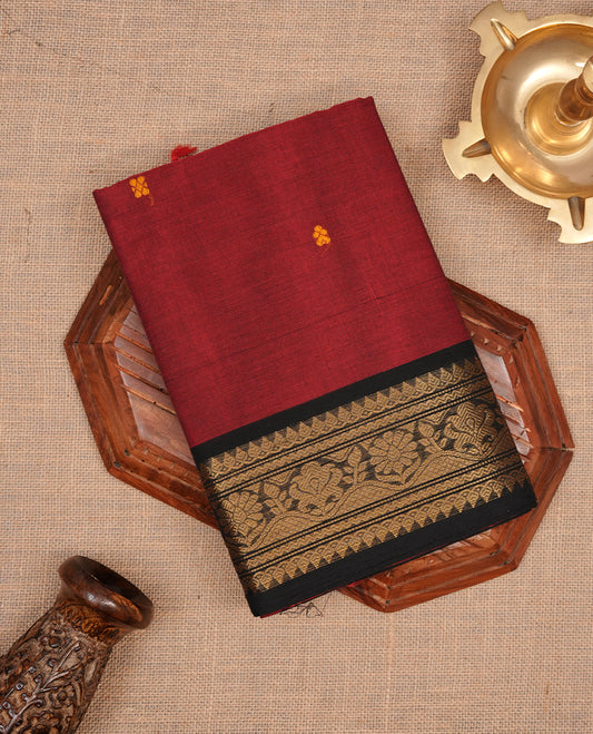 Maroon colour chettinad saree featuring gold zari motifs on body, complemented by contrast black colour with traditional border, paired with matching blouse piece.