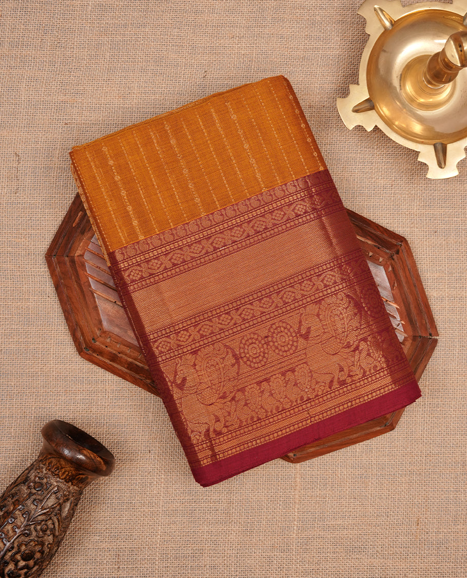 Mustard colour chettinad saree featuring gold zari stripes on body, complemented by contrast Maroon colour with traditional border, paired with matching blouse piece.