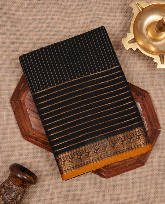 Black colour chettinad cotton saree featuring gold zari stripes on body, complemented by yellow piping with gold zari border, paired with matching blouse piece.
