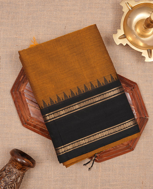 Bronze colour chettinad cotton saree featuring elegant plain body, complemented by contrast black with gold zari border, paired with matching blouse piece.