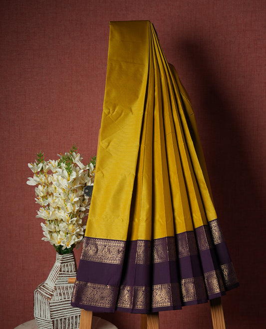 Olive yellow colour Semi Silk Saree with gold zari striped patterns on the body, paired with a contrasting Dark purple traditional pallu and border, and a matching blouse piece.