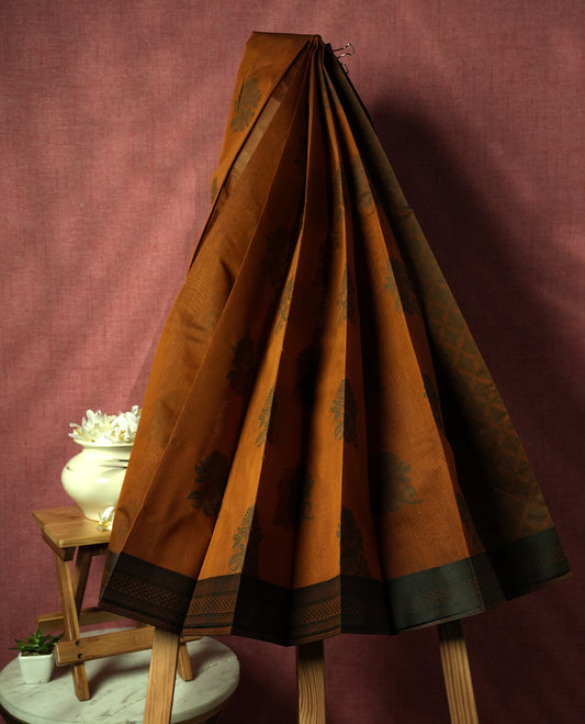 Deep mustard colour silk cotton saree featuring subtle elegant floral woven motifs on the body, complemented by a classic contrast border and pallu with intricate traditional detailing & Comes with a matching blouse piece.