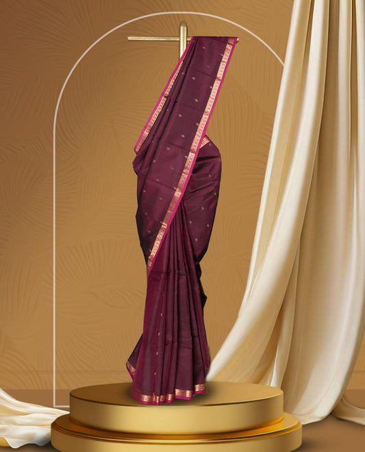 Dark maroon colour soft silk saree with subtle golden buttas, accentuated by a pink zari border and pallu & Paired with a matching blouse.