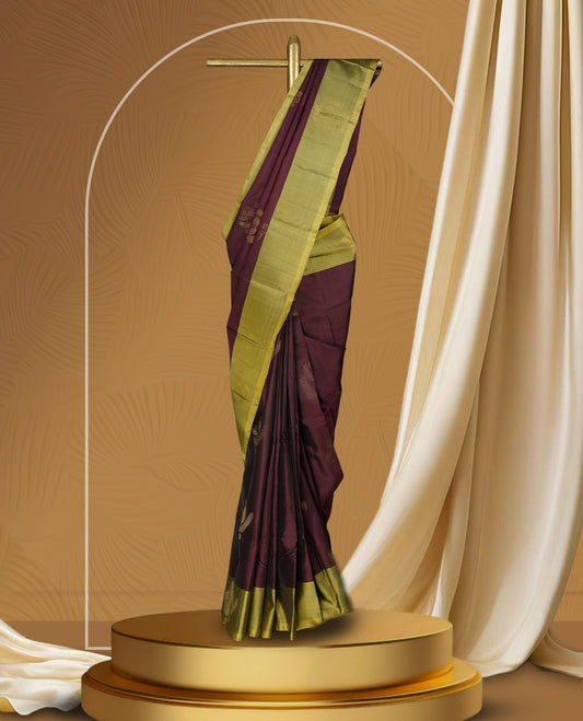 Maroon colour soft silk saree adorned with small golden buttas, enhanced by a shimmering light olive green zari border and pallu with delicate motifs & paired with a matching blouse.