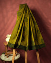 Olive green colour silk cotton saree featuring subtle woven motifs throughout the body, enhanced by a striking contrast border and an intricately designed pallu with floral patterns &  Comes with a matching blouse piece.