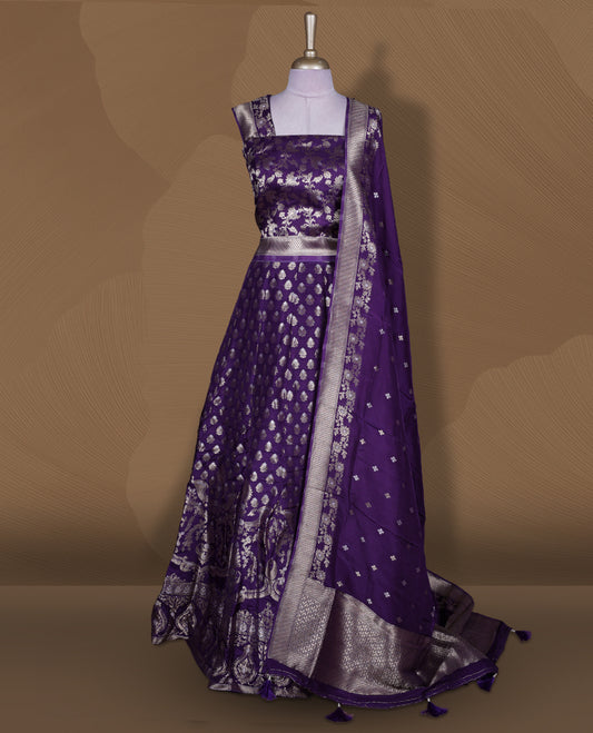 Purple colour Banarasi lehenga set with a stitched flared lehenga featuring all‑over zari butti motifs and rich woven border, paired with an unstitched floral zari blouse piece and matching dupatta with zari border and tasselled edges.