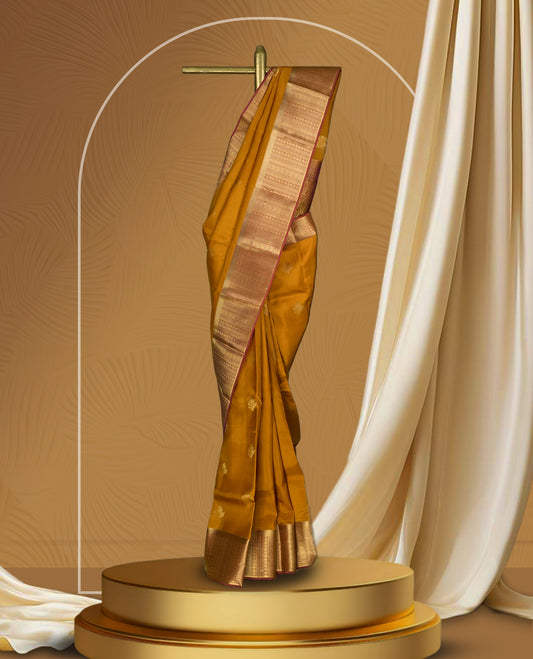 Ochre yellow colour soft silk saree adorned with small golden buttas, enhanced by a rich gold zari border and pallu with intricate detailing & paired with a matching blouse.
