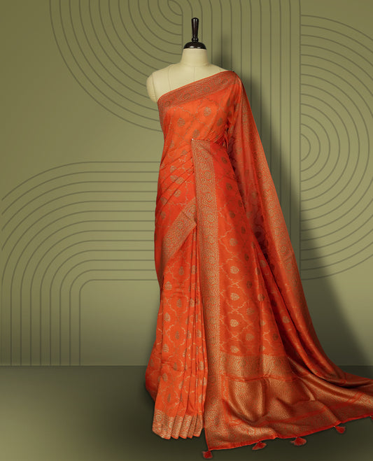 Orange colour semi Banarasi Tussar Georgette saree with gold zari motifs on the body, a grand woven golden pallu, and ornate zari border. Includes a matching blouse piece for a complete look.