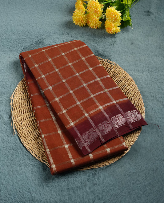 Brown colour Chettinad cotton saree featuring a silver zari checkered body, paired with a contrast maroon pallu highlighted by a silver zari floral border, and a matching maroon checkered blouse piece with silver zari detailing.