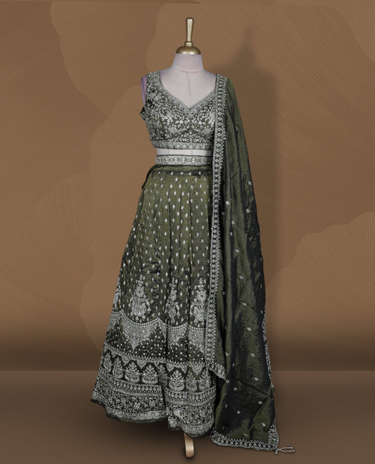 Olive green and black ombre effect lehenga set with stitched sleeveless V‑neck heavily embroidered blouse, matching stitched flared lehenga featuring intricate zari and sequin borders, and coordinated dupatta with embellished edge.