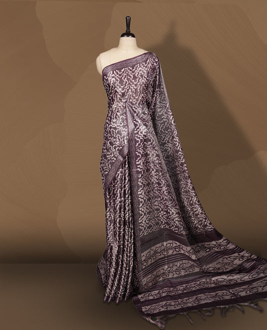 Chocolate colour semi jute tissue saree featuring intricate wave motifs all over the body, enhanced with a shimmering zari striped pallu, woven border, and matching blouse piece.