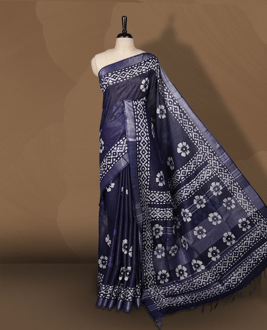 Navy blue colour semi jute tissue saree featuring white floral prints across the body, adorned with intricate geometric woven borders and a graceful floral work pallu & Comes with a matching blouse piece.