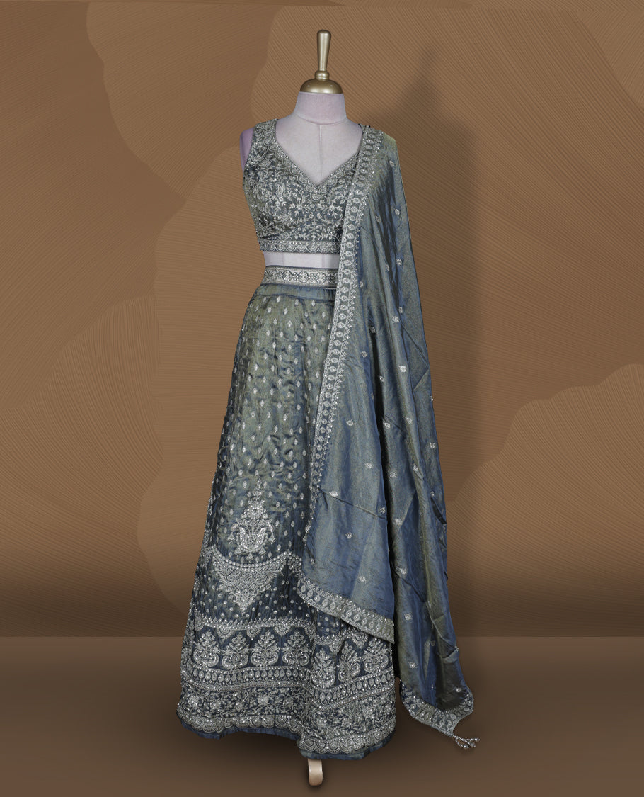 Steel grey and olive ombre effect lehenga set with stitched sleeveless V‑neck embroidered blouse, matching stitched flared lehenga featuring heavy zari and sequin work, and coordinated dupatta with embellished border.