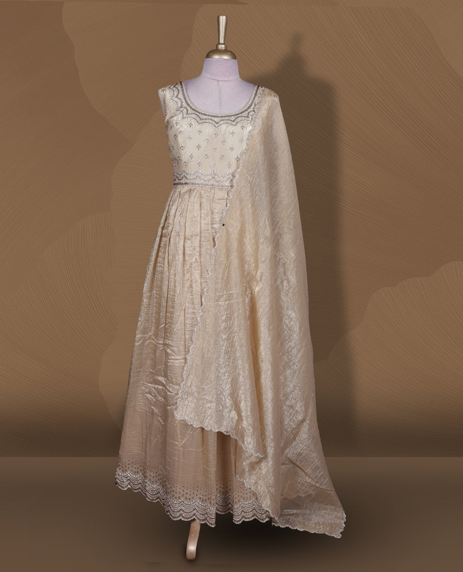 Champagne beige colour stitched gown set with sleeveless embroidered yoke, flared ankle‑length silhouette, and attached dupatta featuring delicate butti work and scalloped beaded edging.