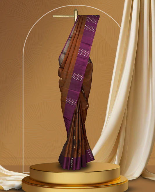 Brown colour soft silk saree adorned with tiny golden buttas, complemented by a rich purple border and pallu with elegant zari designs & Paired with a matching blouse.