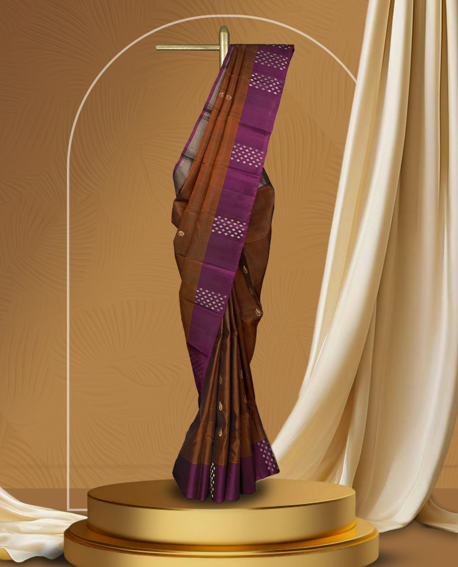 Brown colour soft silk saree adorned with tiny golden buttas, complemented by a rich purple border and pallu with elegant zari designs & Paired with a matching blouse.