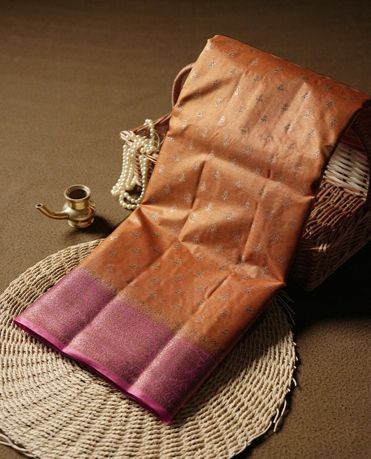 Copper toned colour pure banarasi tussar saree adorned with subtle silver zari motifs all over, complemented by a rich contrast magenta Banarasi border & Comes with a matching blouse piece.
