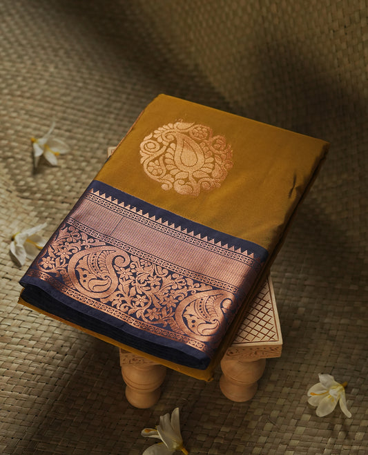 Dark mustard colour Semi Silk Saree with copper zari motifs on the body, paired with a contrast Dark blue colour pallu with copper zari traditioal border, and a matching blouse piece.