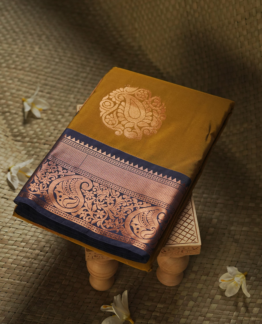 Dark mustard colour Semi Silk Saree with copper zari motifs on the body, paired with a contrast Dark blue colour pallu with copper zari traditioal border, and a matching blouse piece.