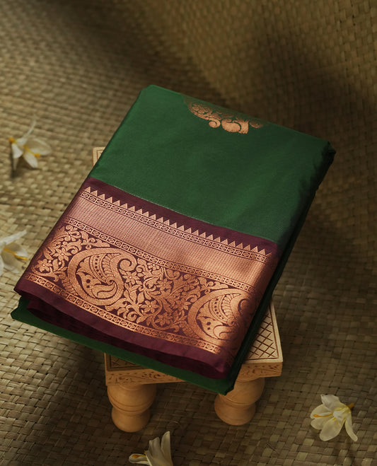 Dark green colour Semi Silk Saree with copper zari motifs on the body, paired with a contrast chocolate brown colour pallu with copper zari traditioal border, and a matching blouse piece.
