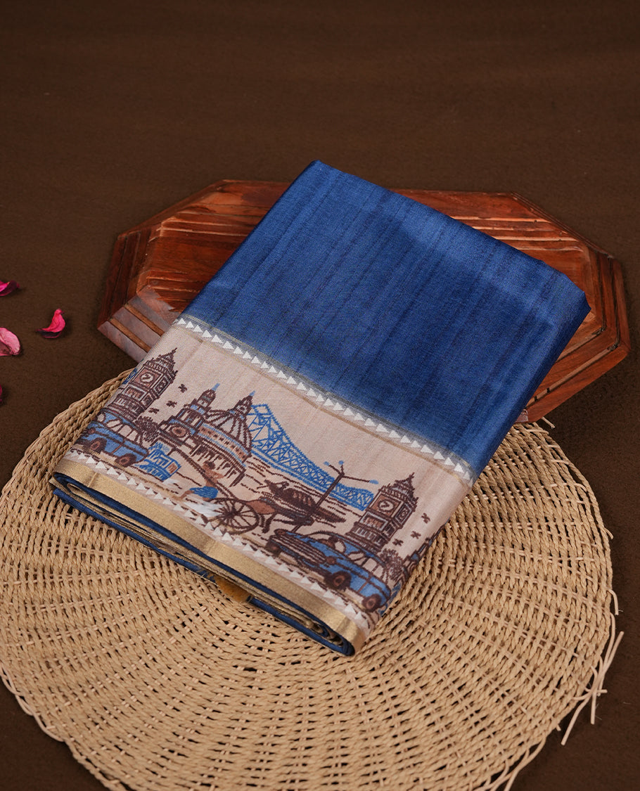 Blue colour semi tusser silk saree featuring contrast cream colour London bridge printed pattern border and paired with matching blouse.