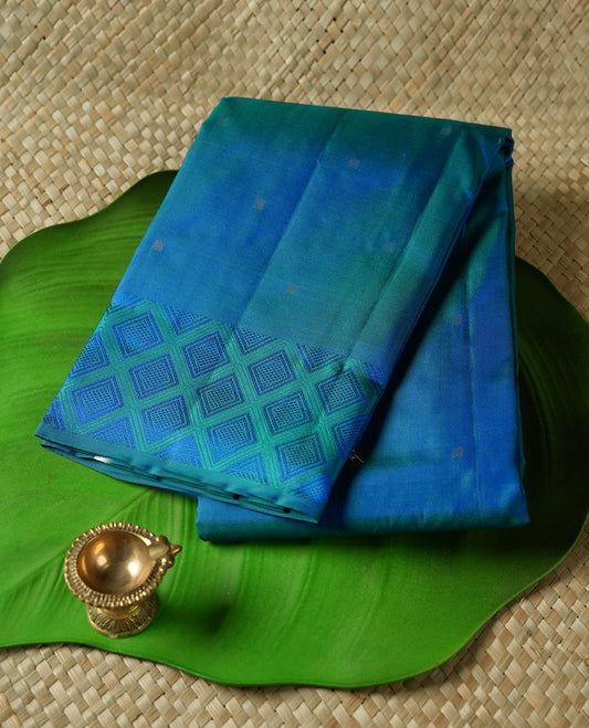 Teal colour Vasundhara silk saree adorned with all-over silver square motifs on the body, complemented by a green & blue box pattern border and paired with a matching blouse piece.