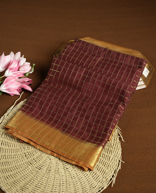 Dark Choclate colour mysore crepe saree with gold zari check pattern on body, complemented by contrast dark mustard colour border featuring peacock and chakkram motifs, paired with matching blouse.
